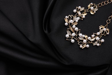 Photo of Beautiful bracelet with pearls on black cloth, top view. Space for text