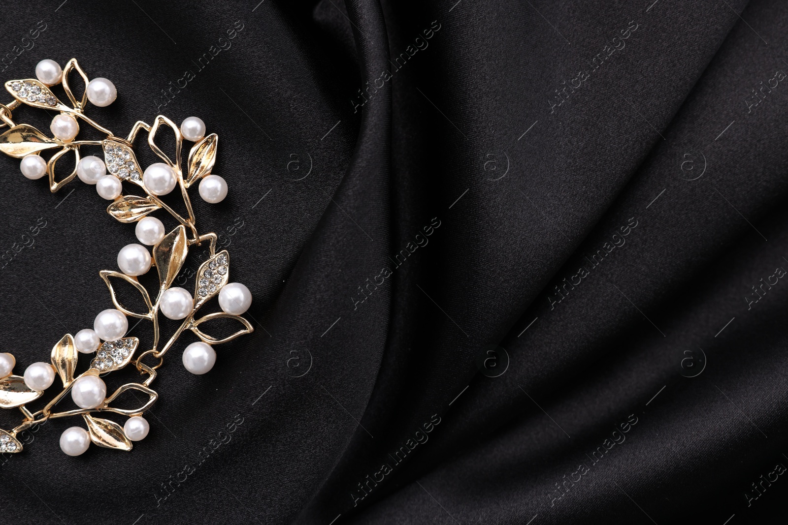 Photo of Beautiful bracelet with pearls on black cloth, top view. Space for text