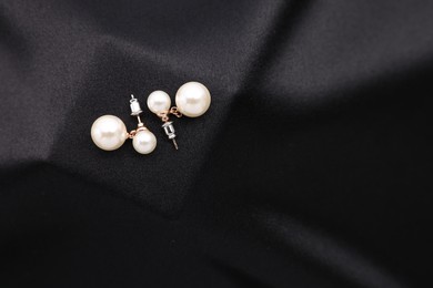 Photo of Beautiful pearl earrings on black cloth, top view. Space for text