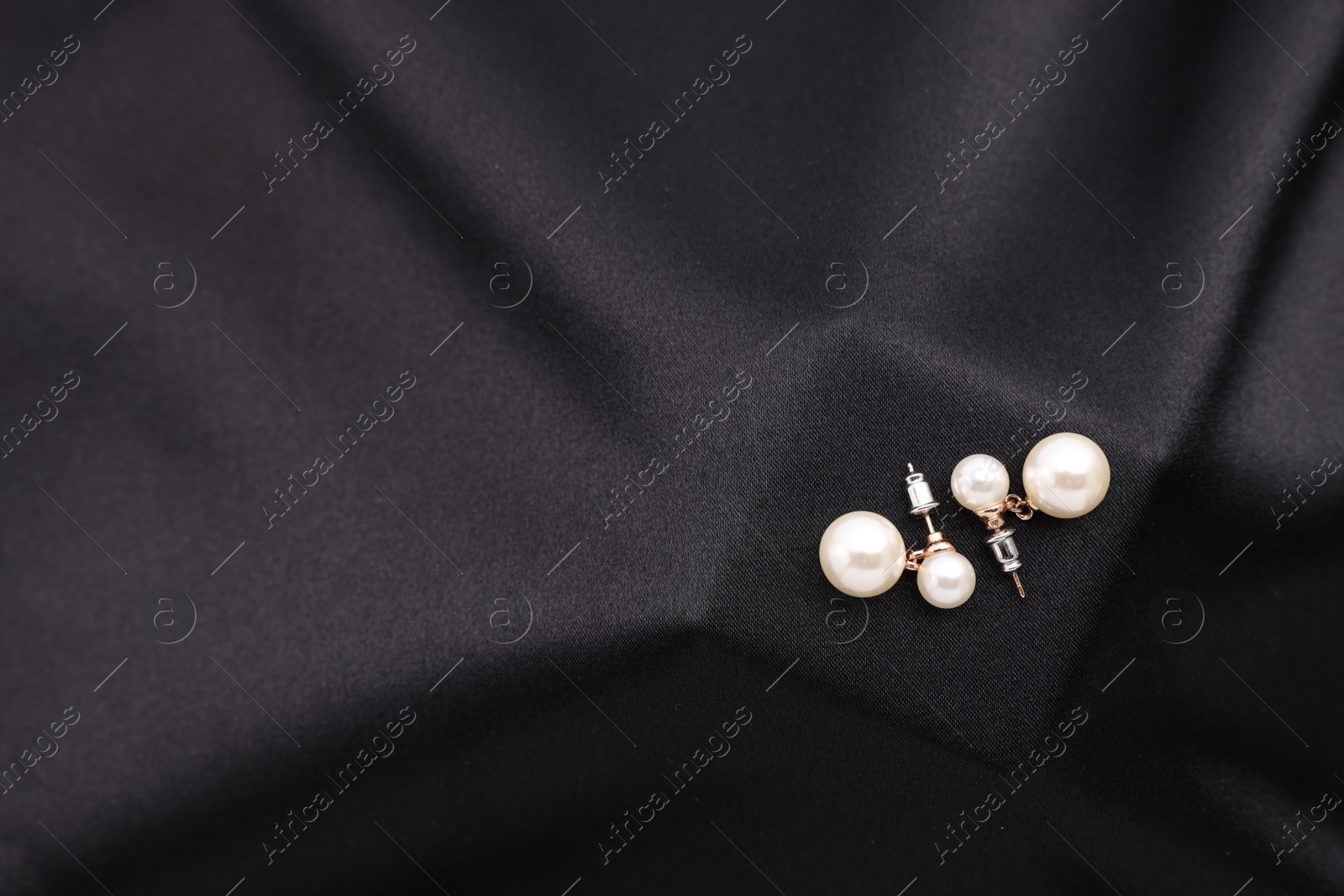 Photo of Beautiful pearl earrings on black cloth, top view. Space for text