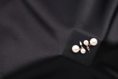 Photo of Beautiful pearl earrings on black cloth, top view. Space for text