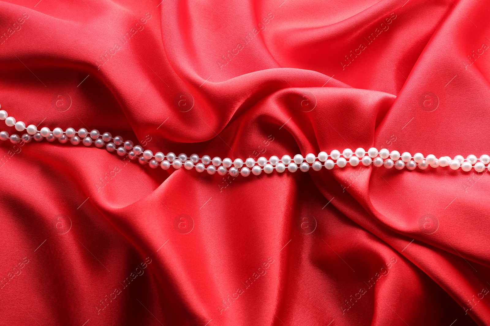 Photo of Beautiful pearl necklace on red cloth, top view