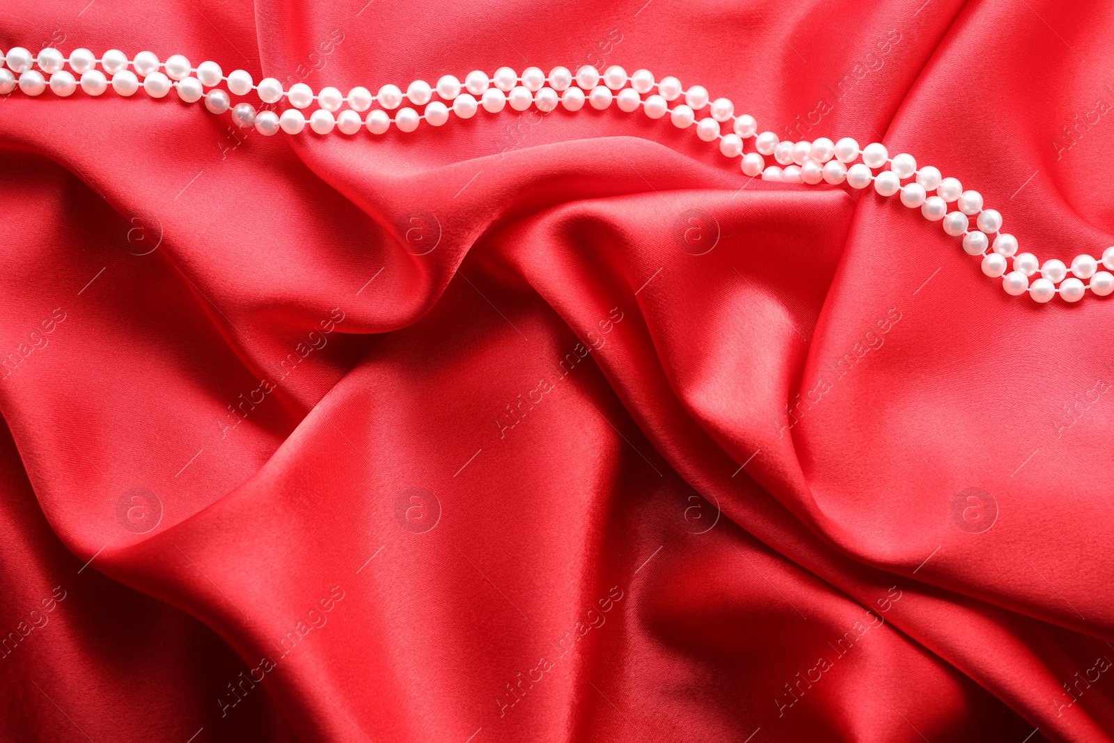 Photo of Beautiful pearl necklace on red cloth, top view. Space for text