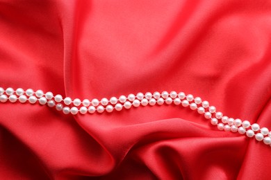 Photo of Beautiful pearl necklace on red cloth, top view