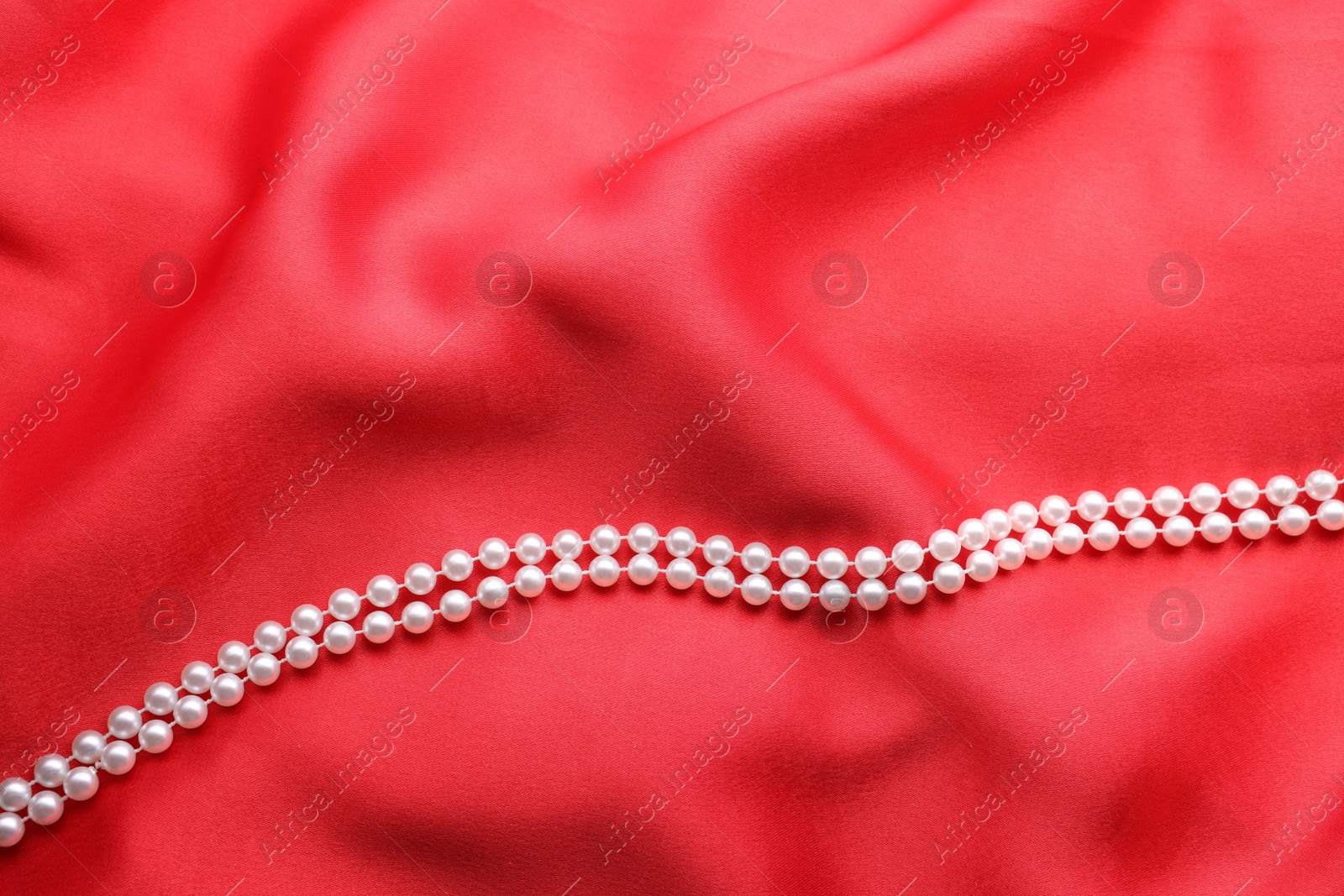 Photo of Beautiful pearl necklace on red cloth, top view