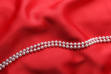 Photo of Beautiful pearl necklace on red cloth, top view