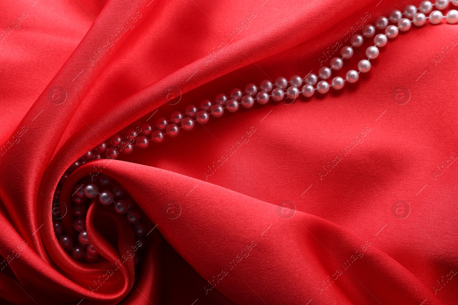 Photo of Beautiful pearl necklace on red cloth, above view