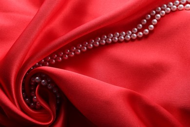 Photo of Beautiful pearl necklace on red cloth, above view