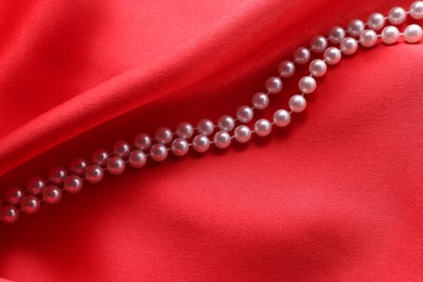 Photo of Beautiful pearl necklace on red cloth, above view