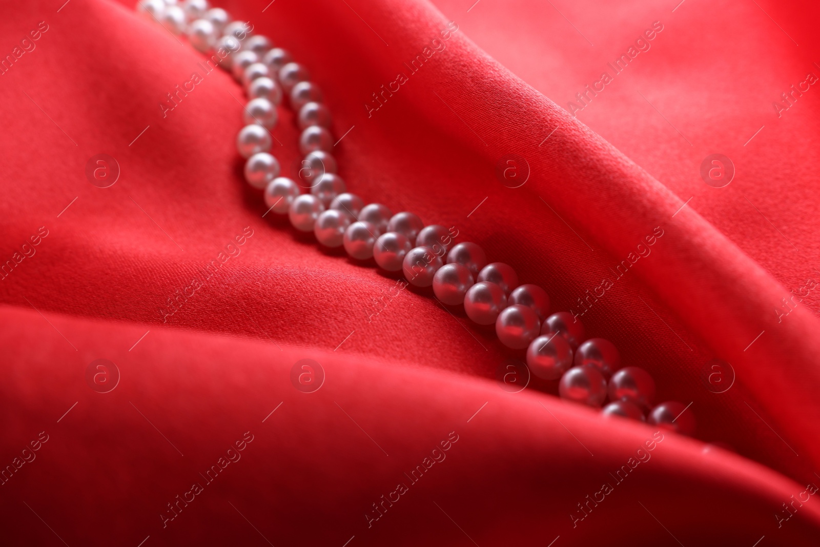 Photo of Beautiful pearl necklace on red cloth, closeup