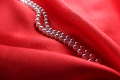 Photo of Beautiful pearl necklace on red cloth, closeup