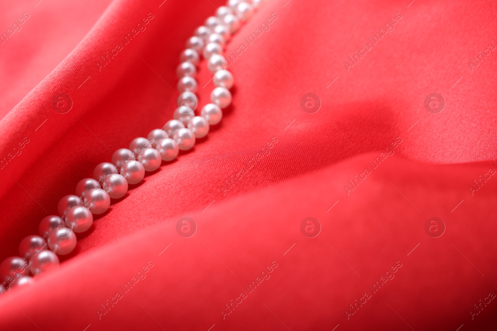 Photo of Beautiful pearl necklace on red cloth, closeup. Space for text