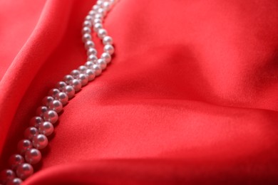 Photo of Beautiful pearl necklace on red cloth, closeup. Space for text