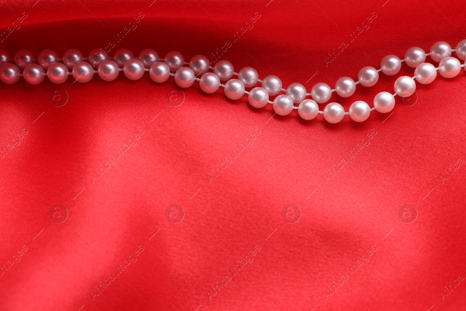 Photo of Beautiful pearl necklace on red cloth, top view. Space for text