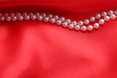 Photo of Beautiful pearl necklace on red cloth, top view. Space for text