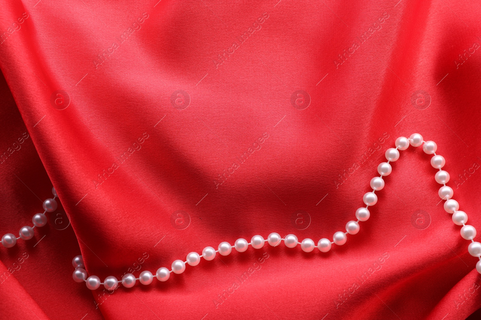 Photo of Beautiful pearl necklace on red cloth, top view. Space for text