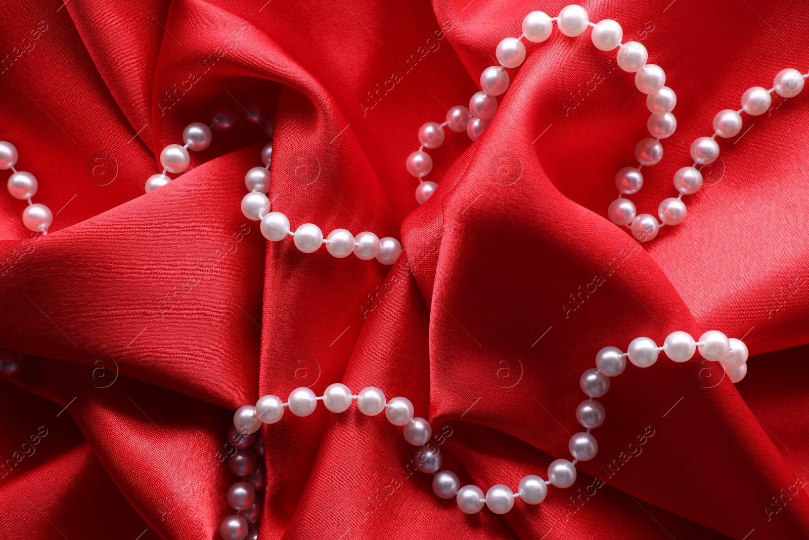 Photo of Beautiful pearl necklace on red cloth, top view