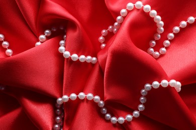 Photo of Beautiful pearl necklace on red cloth, top view