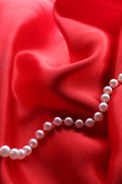 Photo of Beautiful pearl necklace on red cloth, top view