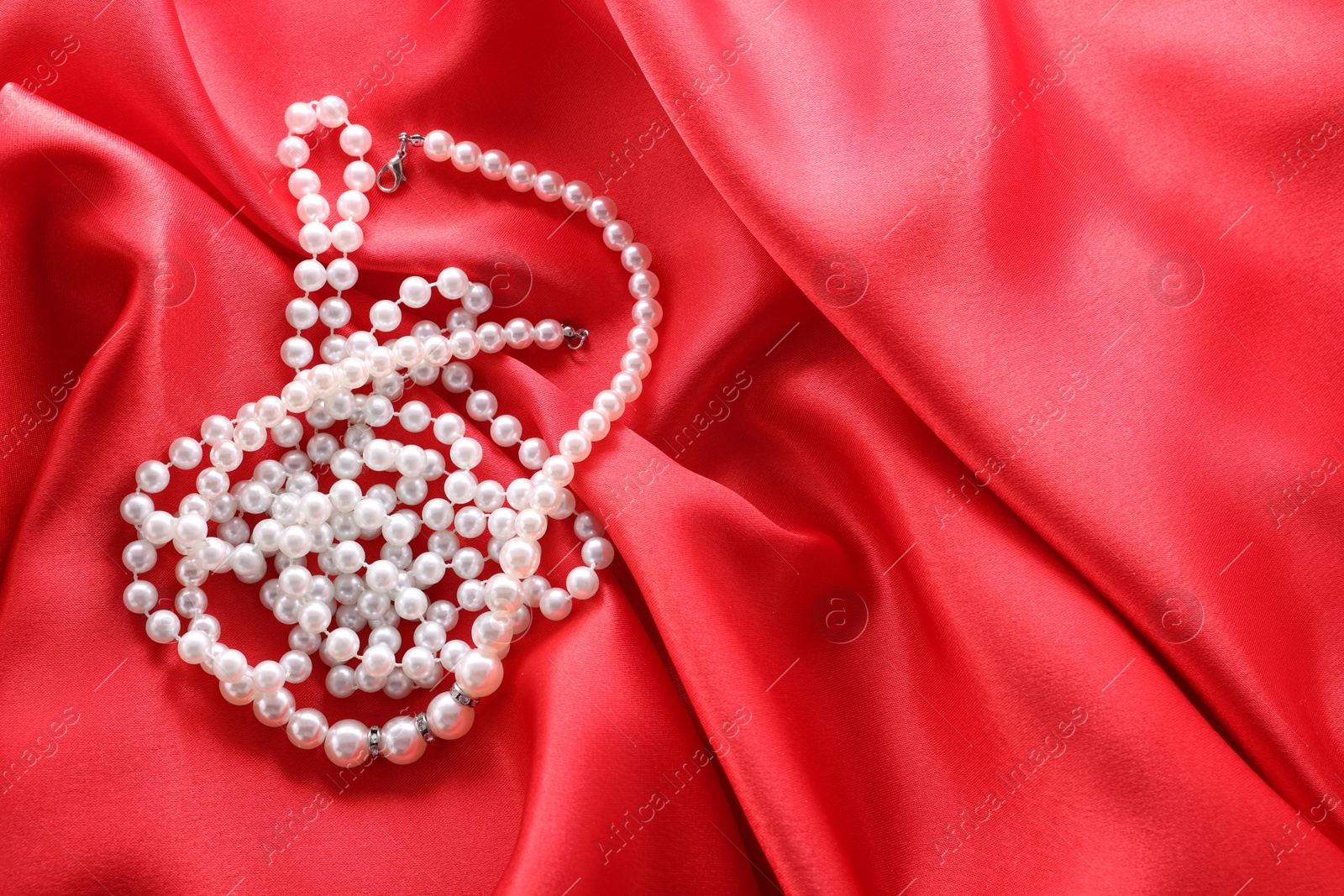 Photo of Beautiful bijouterie with pearls on red cloth, top view. Space for text