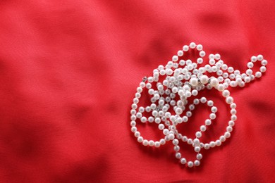 Photo of Beautiful bijouterie with pearls on red cloth, top view. Space for text