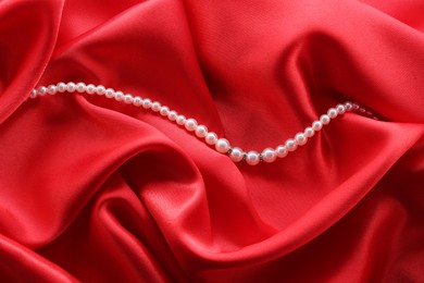 Photo of Beautiful pearl necklace on red cloth, top view