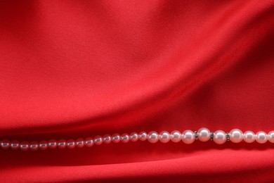 Photo of Beautiful pearl necklace on red cloth, top view. Space for text