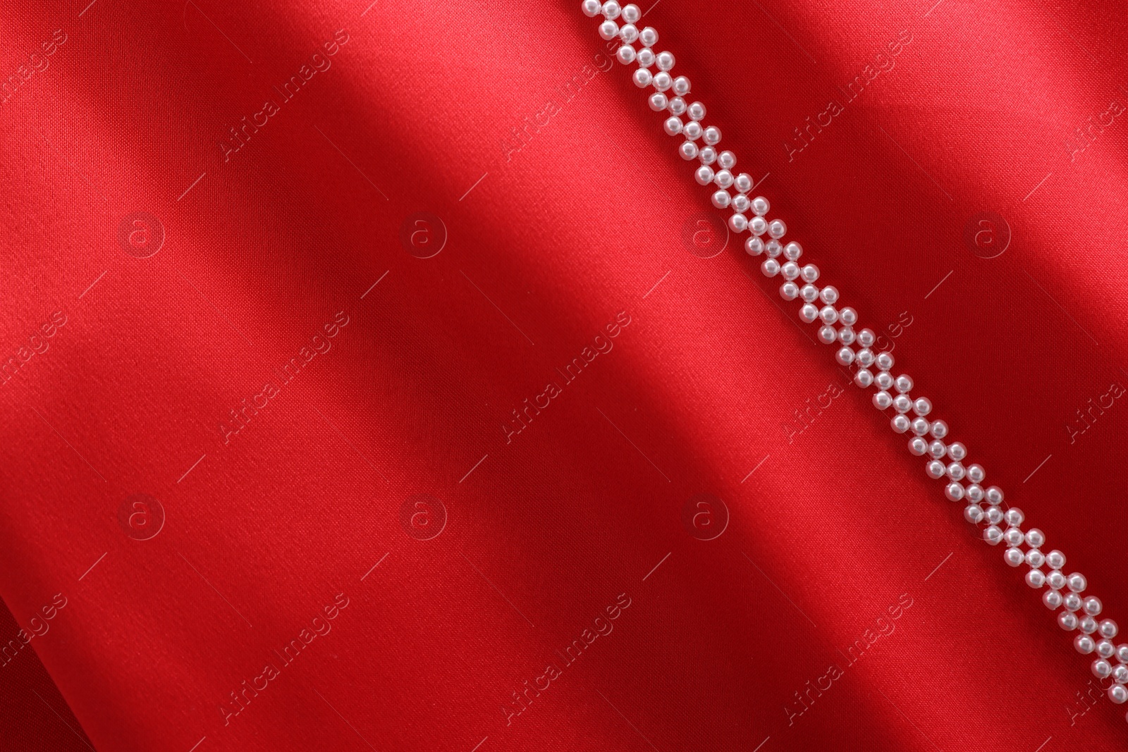 Photo of Beautiful pearl necklace on red cloth, top view. Space for text