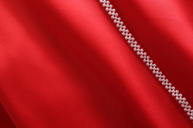 Photo of Beautiful pearl necklace on red cloth, top view. Space for text