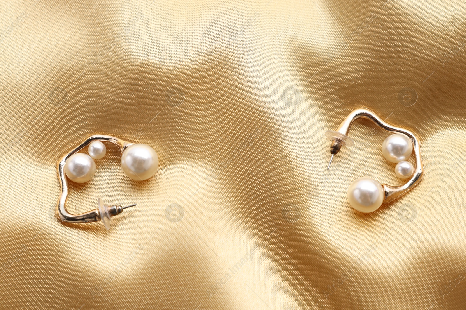 Photo of Beautiful pearl earrings on golden silk, top view