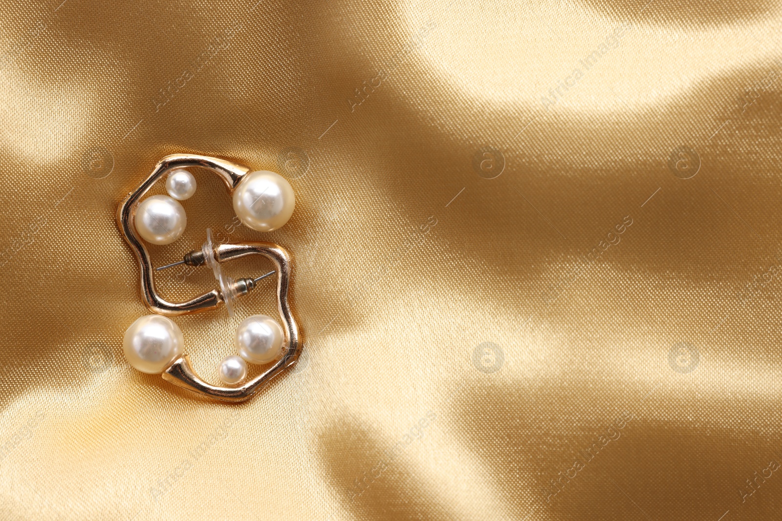 Photo of Beautiful pearl earrings on golden silk, top view. Space for text