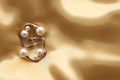 Photo of Beautiful pearl earrings on golden silk, top view. Space for text