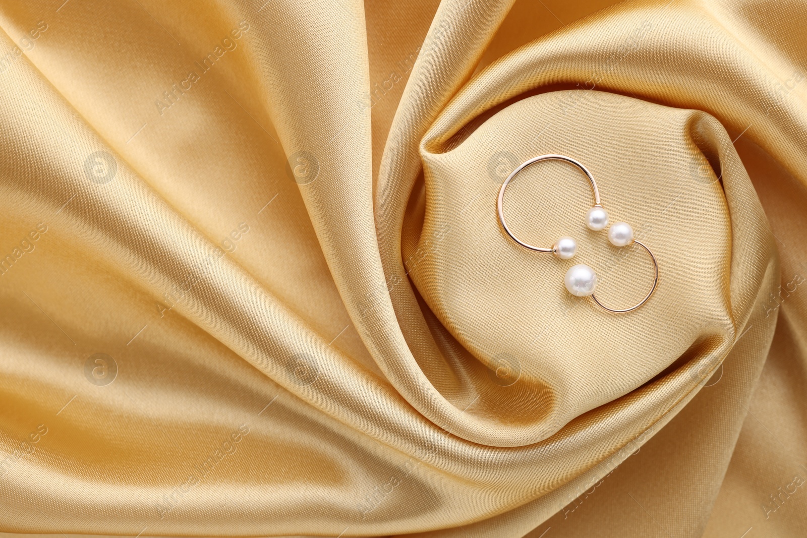 Photo of Beautiful pearl jewelry on golden silk, top view. Space for text