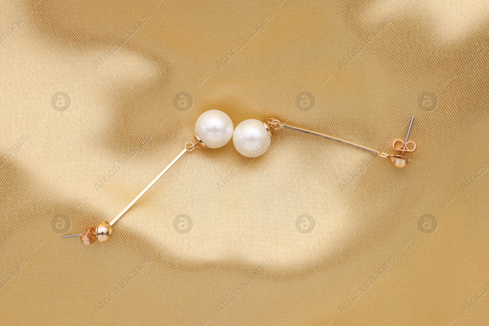 Photo of Beautiful pearl earrings on golden silk, top view