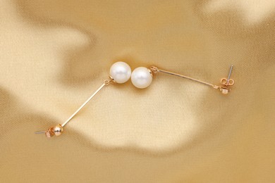 Photo of Beautiful pearl earrings on golden silk, top view