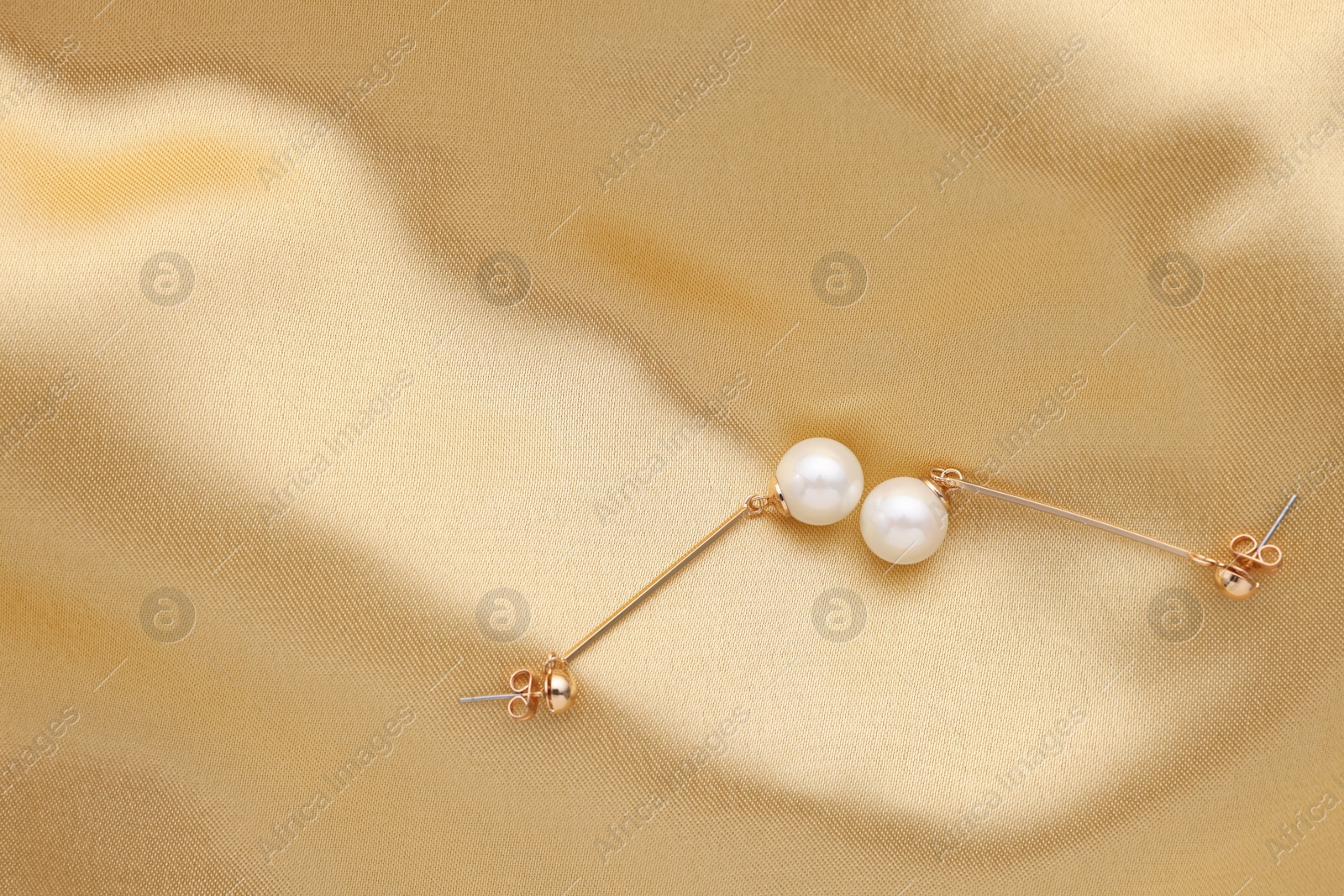 Photo of Beautiful pearl earrings on golden silk, top view. Space for text