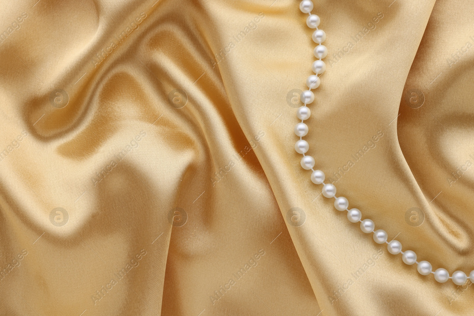 Photo of Beautiful pearl necklace on golden silk, top view. Space for text