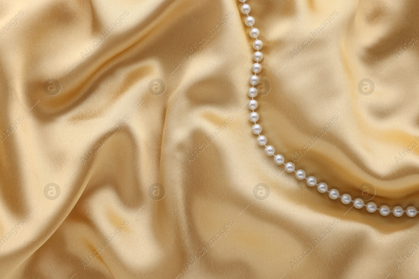 Photo of Beautiful pearl necklace on golden silk, top view. Space for text