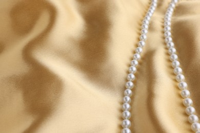 Photo of Beautiful pearl necklace on golden silk, closeup. Space for text