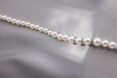 Photo of Beautiful pearl necklace on grey silk, above view