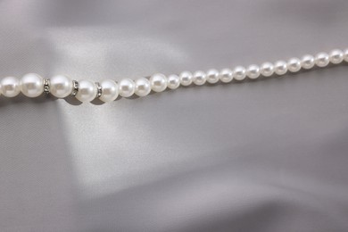 Photo of Beautiful pearl necklace on grey silk, above view