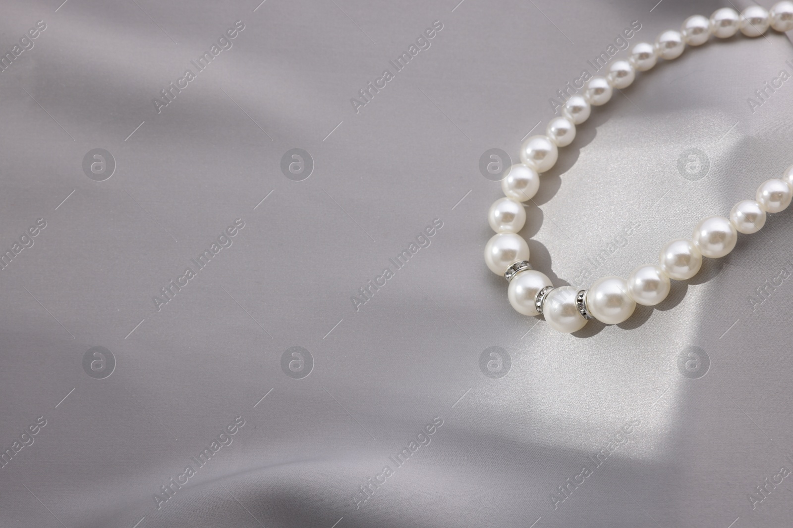 Photo of Beautiful pearl necklace on grey silk, closeup. Space for text