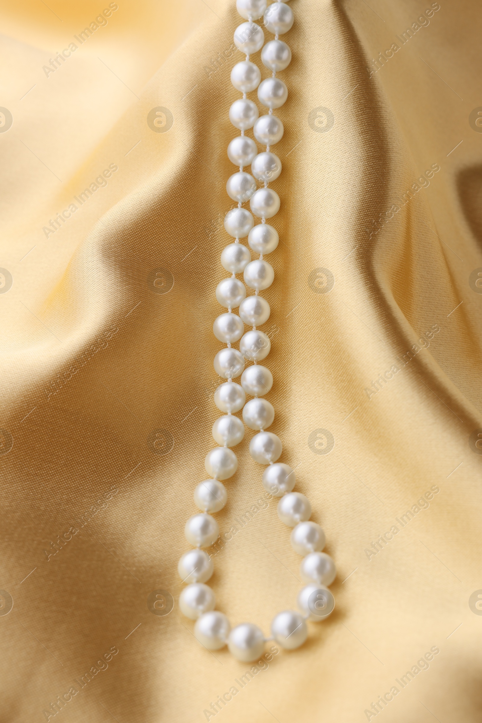 Photo of Beautiful pearl necklace on golden silk, above view