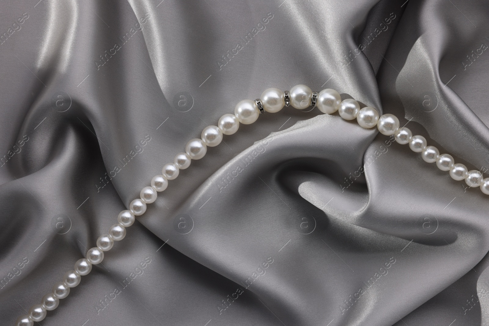 Photo of Beautiful pearl necklace on grey silk, top view