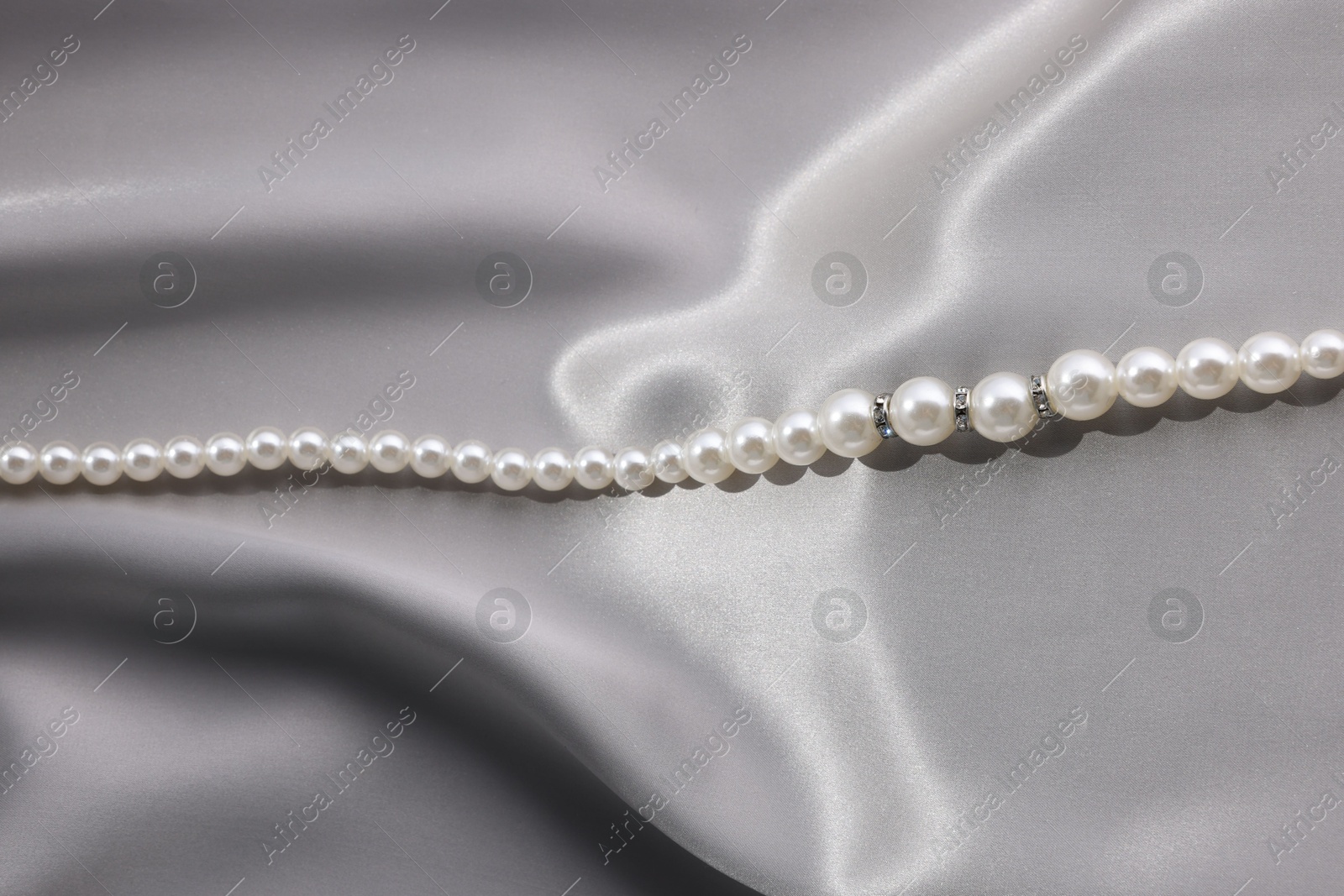 Photo of Beautiful pearl necklace on grey silk, above view