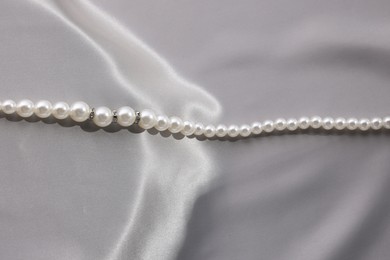 Photo of Beautiful pearl necklace on grey silk, above view