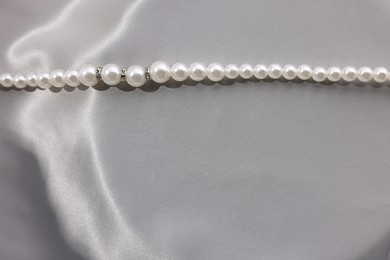 Photo of Beautiful pearl necklace on grey silk, top view