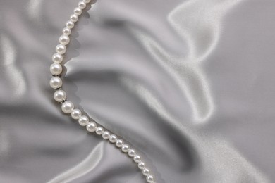 Photo of Beautiful pearl necklace on grey silk, top view. Space for text