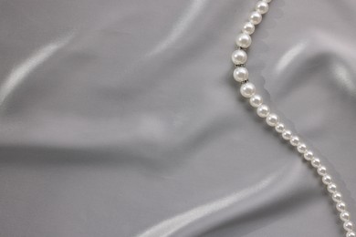 Photo of Beautiful pearl necklace on grey silk, top view. Space for text