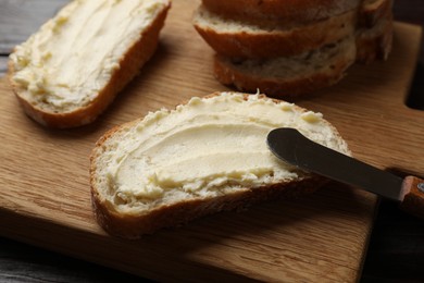 Photo of Fresh bread with butter and knife on wooden board, closeup